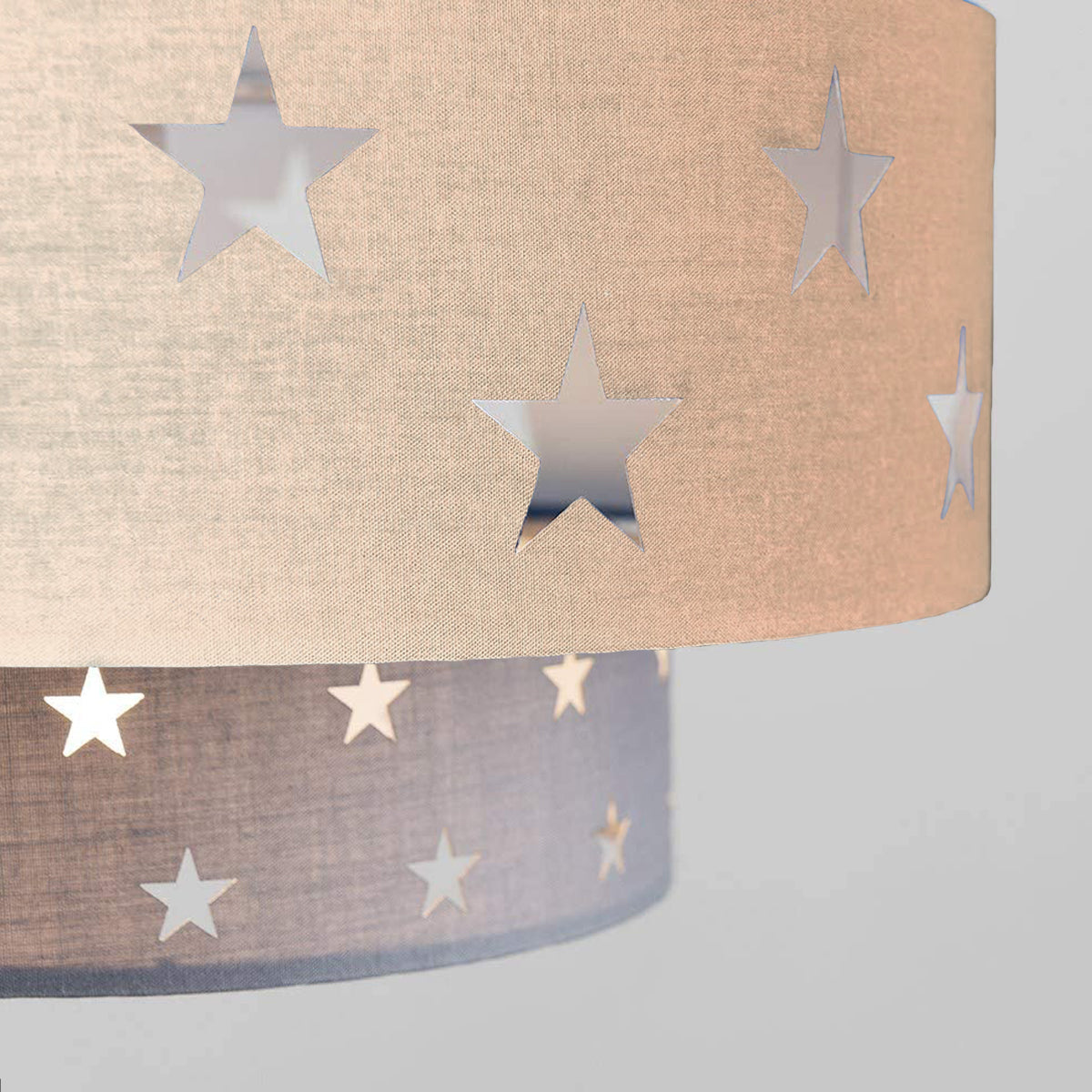 Our Grey and Cream two tiered star shade features a mixture of large and small sweet stars cut out across a grey and cream background. When your lamp is turned on it will shine out through these cut-outs, mimicking a beautiful night sky. This lampshade is made with soft-touch fabric for a little bit of luxury.